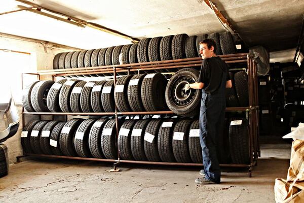 Mitarbeiter in Werkstatt lagert Autoreifen auf Regal, Reifenlager und Reifenservice.