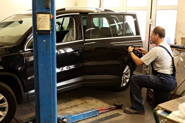 Ein Mechaniker repariert in einer Autowerkstatt die Tür eines schwarzen Fahrzeugs.