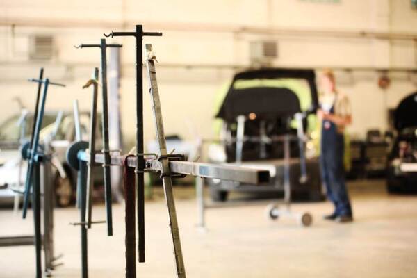 In einer Autowerkstatt steht ein Mechaniker vor einem Auto mit geöffneter Motorhaube.