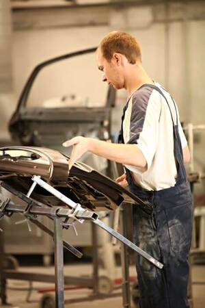 Automechaniker lackiert Autotür in Werkstatt, Karosseriebau und Fahrzeugreparatur.