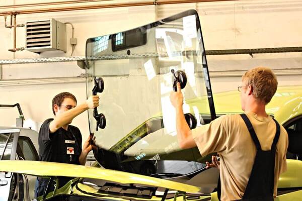 Zwei Automechaniker tauschen in einer Werkstatt eine Windschutzscheibe am Auto aus.