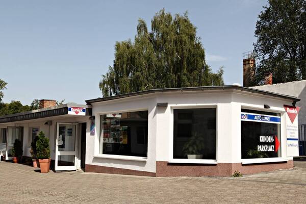Helles Autohaus mit großem Kundenparkplatz, vielen Fenstern und gepflegten Pflanzen vor dem Eingang.